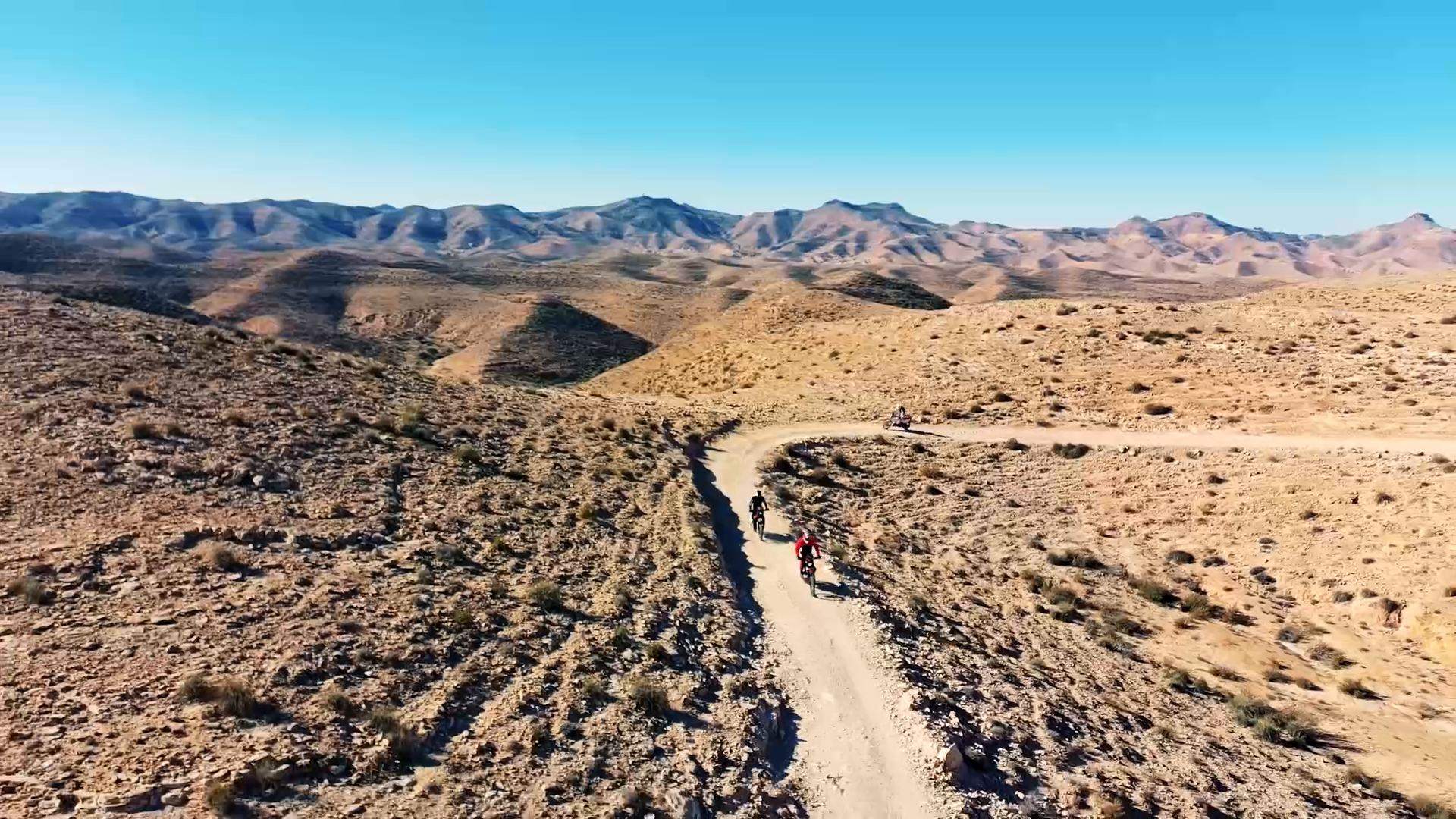 Due moto su una pista tra le montagne del deserto, viste dall'alto