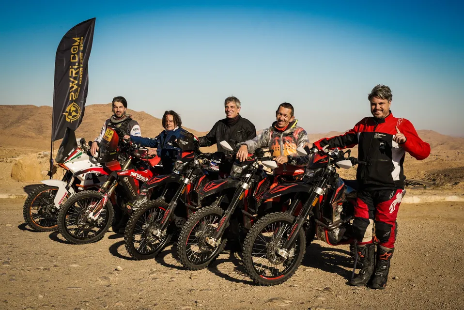 Il gruppo con la bandiera 2WRI.COM tra le colline del deserto, sorridente accanto alle moto