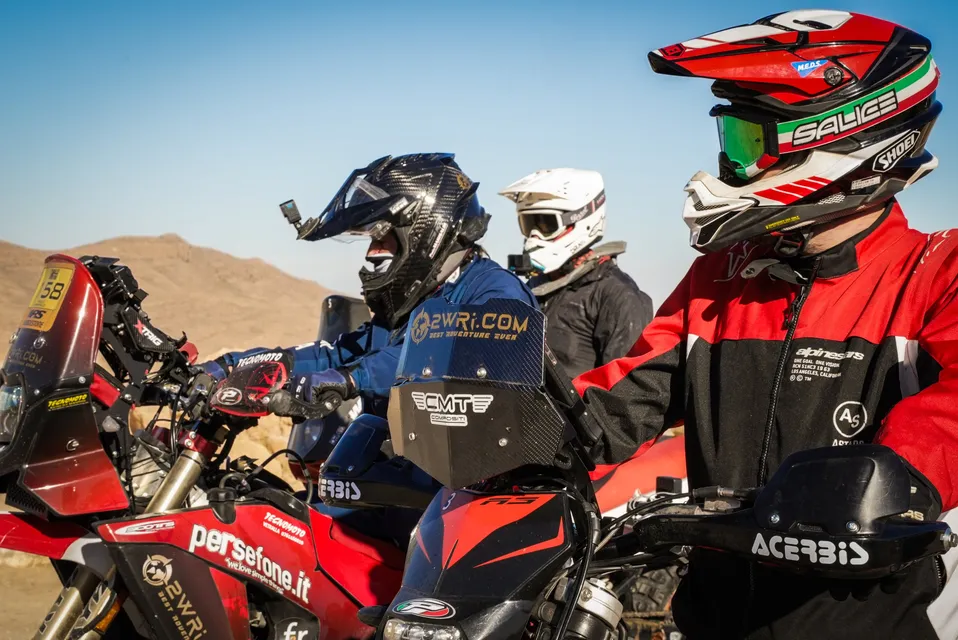 Tre piloti in primo piano sulle moto, con le montagne alle spalle