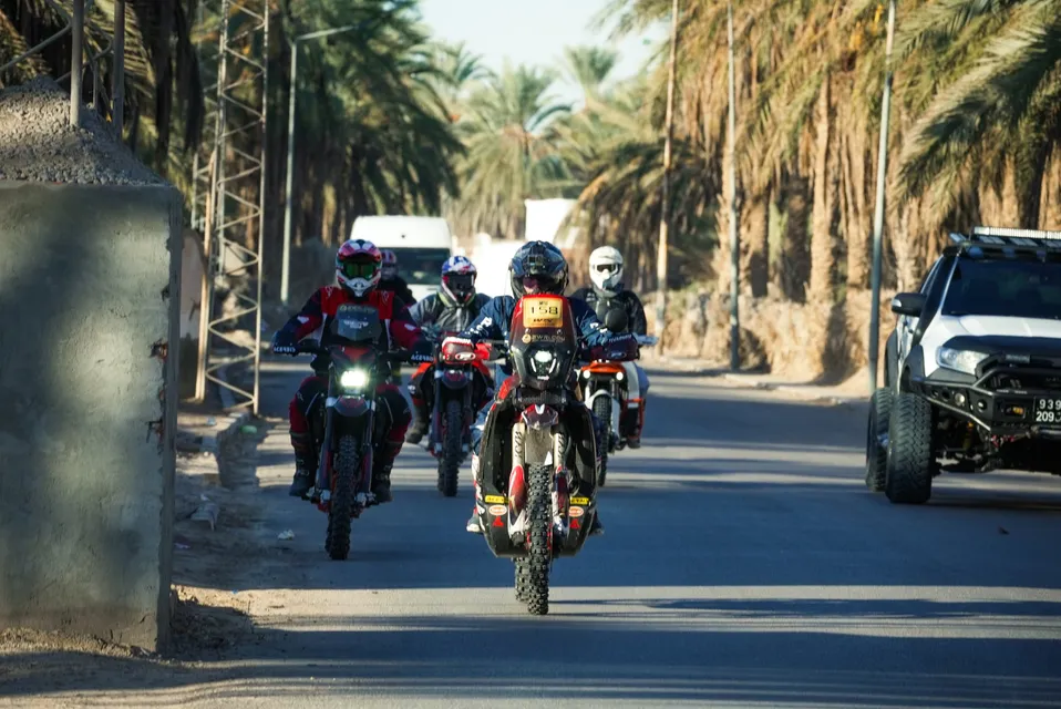 Il gruppo di moto attraversa una strada tra le palme di un'oasi