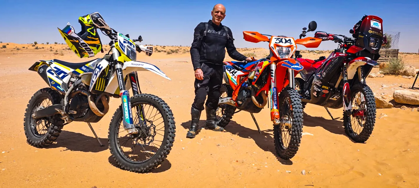 Un pilota in piedi tra tre moto nel deserto