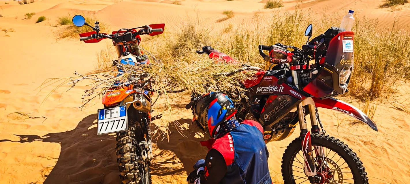 Un pilota si occupa della moto tra i cespugli e le dune
